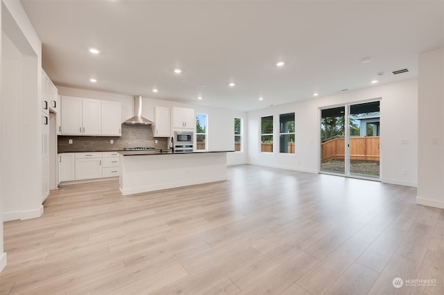 kitchen with white cabinets, light wood-type flooring, stainless steel microwave, and wall chimney range hood