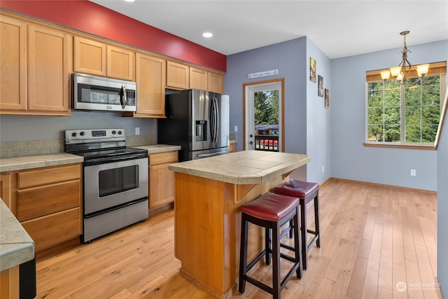 kitchen featuring an inviting chandelier, pendant lighting, appliances with stainless steel finishes, light hardwood / wood-style floors, and a center island