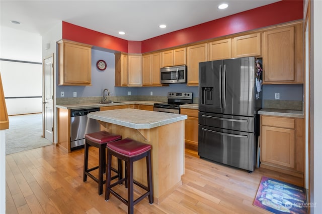 kitchen with light hardwood / wood-style flooring, a kitchen bar, stainless steel appliances, a center island, and sink