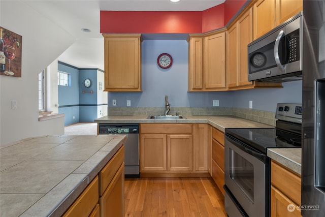 kitchen with light hardwood / wood-style flooring, tile countertops, stainless steel appliances, sink, and ornamental molding