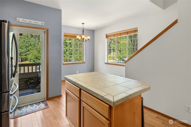 kitchen featuring an inviting chandelier, decorative light fixtures, light hardwood / wood-style floors, stainless steel refrigerator, and a kitchen island