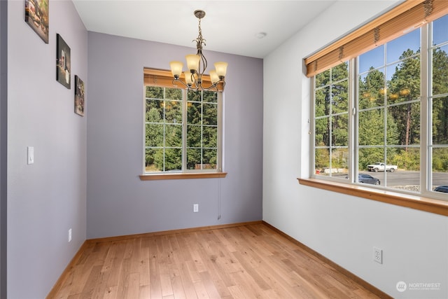 spare room featuring plenty of natural light, an inviting chandelier, and light hardwood / wood-style floors