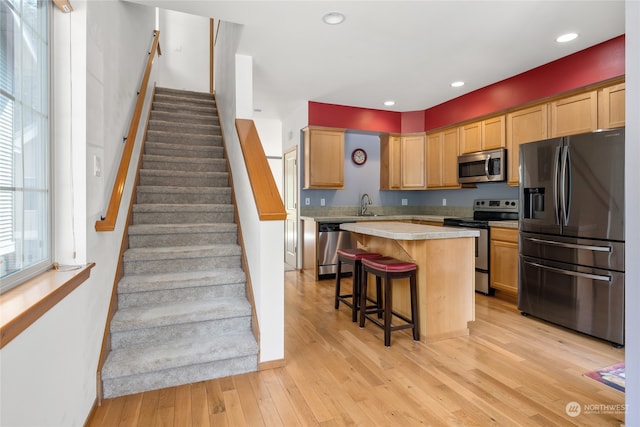 kitchen with a kitchen island, sink, appliances with stainless steel finishes, a breakfast bar area, and light hardwood / wood-style floors