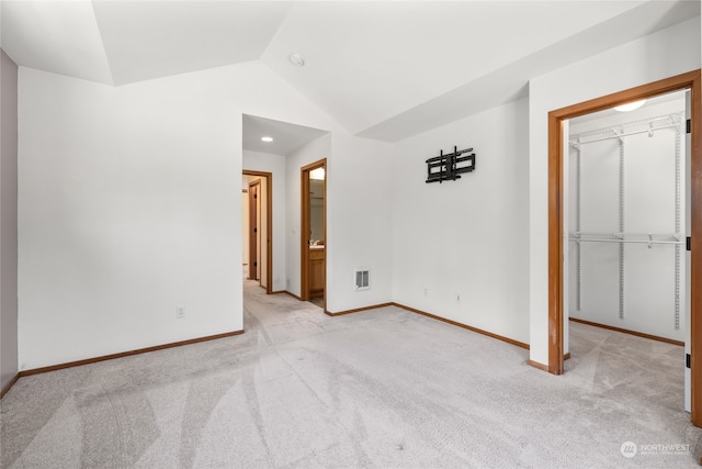 unfurnished bedroom featuring a closet, connected bathroom, light carpet, and vaulted ceiling