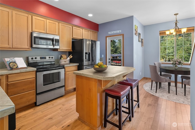 kitchen featuring decorative light fixtures, appliances with stainless steel finishes, light hardwood / wood-style floors, a chandelier, and a kitchen island