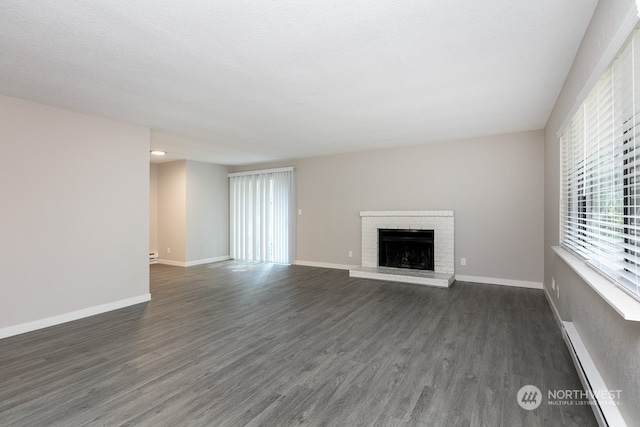 unfurnished living room with a baseboard radiator, dark hardwood / wood-style floors, a textured ceiling, and a brick fireplace