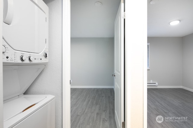 laundry room featuring a baseboard radiator, wood-type flooring, and stacked washer / drying machine