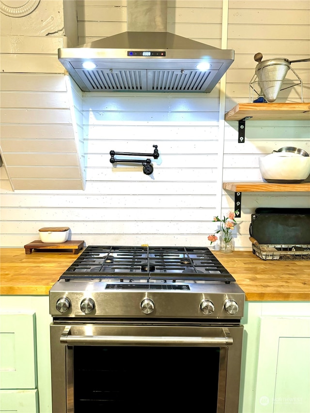 kitchen with high end stainless steel range oven, ventilation hood, wooden walls, and wood counters