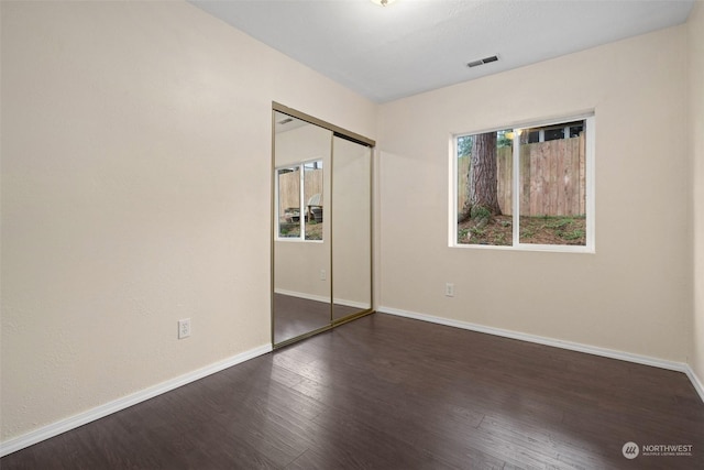 unfurnished bedroom with dark wood-type flooring, a closet, and multiple windows