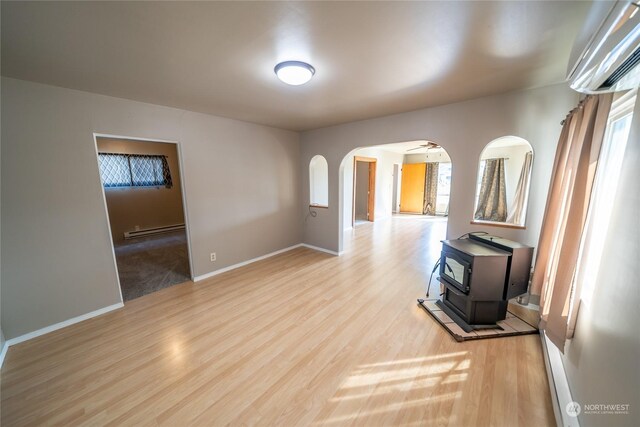 unfurnished living room with a wood stove, a healthy amount of sunlight, a baseboard radiator, and light wood-type flooring