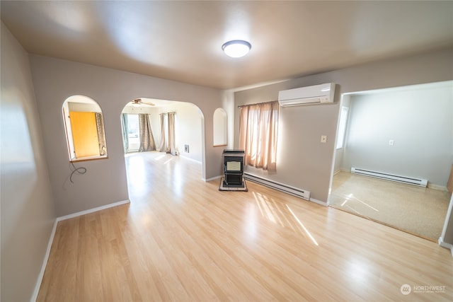 empty room featuring a wood stove, a baseboard radiator, a wall unit AC, and light wood-type flooring