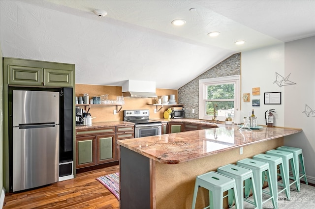 kitchen with stainless steel appliances, light stone counters, kitchen peninsula, a breakfast bar, and vaulted ceiling