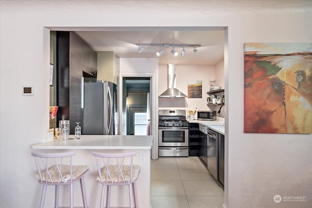 kitchen featuring a breakfast bar area, wall chimney exhaust hood, light tile patterned floors, stainless steel appliances, and kitchen peninsula