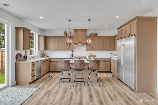 kitchen with light wood-type flooring, under cabinet range hood, a center island, appliances with stainless steel finishes, and a breakfast bar area