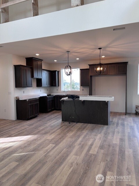 kitchen featuring pendant lighting, light wood-style flooring, a kitchen island, dark brown cabinets, and a chandelier