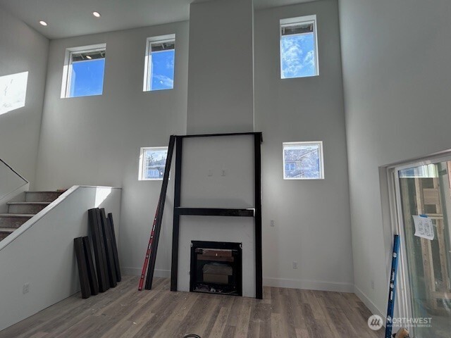 unfurnished living room with recessed lighting, baseboards, a high ceiling, and wood finished floors