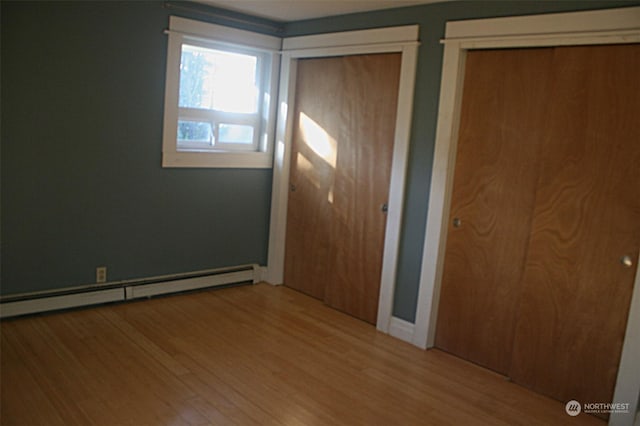 unfurnished bedroom with baseboard heating and wood-type flooring