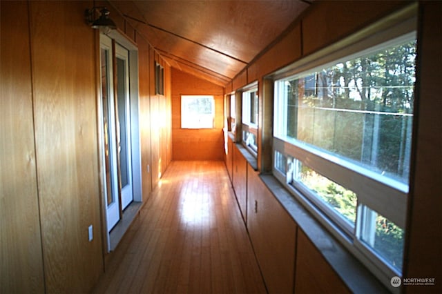 hall featuring lofted ceiling, a healthy amount of sunlight, light wood-type flooring, and wooden walls