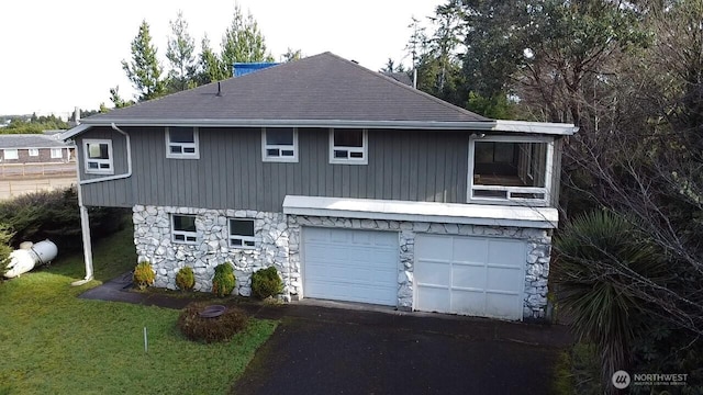 view of front of property featuring stone siding, a front lawn, an attached garage, and aphalt driveway