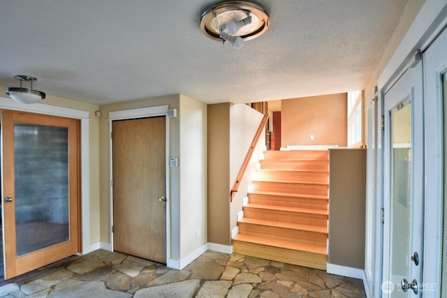 interior space featuring stone finish floor, stairs, baseboards, and a textured ceiling