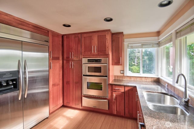 kitchen with a warming drawer, tasteful backsplash, appliances with stainless steel finishes, light wood-style floors, and a sink