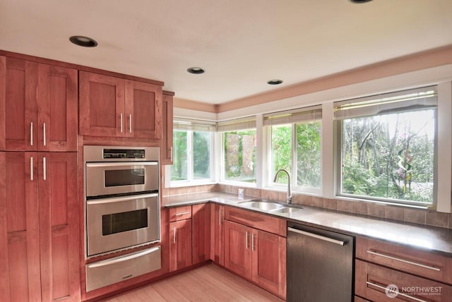 kitchen with a warming drawer, stainless steel appliances, brown cabinetry, a healthy amount of sunlight, and a sink