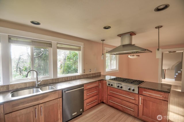 kitchen with brown cabinetry, appliances with stainless steel finishes, hanging light fixtures, island exhaust hood, and a sink