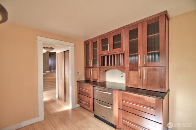 kitchen featuring glass insert cabinets, dark stone counters, brown cabinets, and light wood finished floors