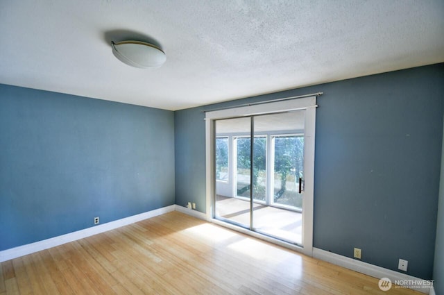 spare room featuring a textured ceiling, wood finished floors, and baseboards