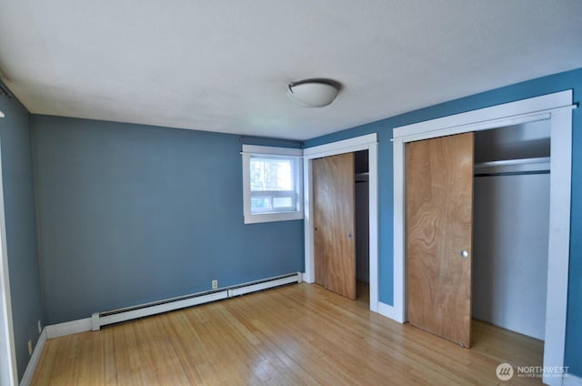 unfurnished bedroom featuring baseboards, a baseboard heating unit, multiple closets, and wood finished floors