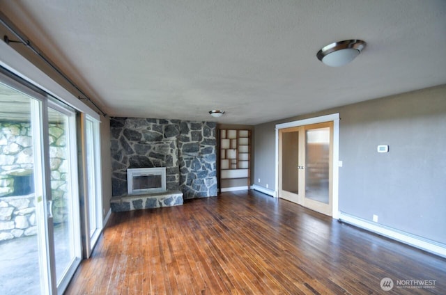 unfurnished living room featuring a baseboard heating unit, a stone fireplace, wood-type flooring, and a baseboard radiator