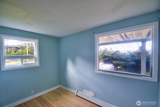 empty room featuring a baseboard radiator, baseboards, and wood finished floors