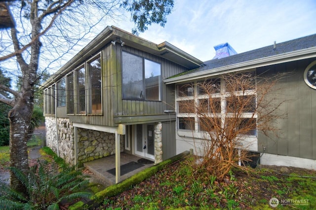 back of house with stone siding, a sunroom, and french doors