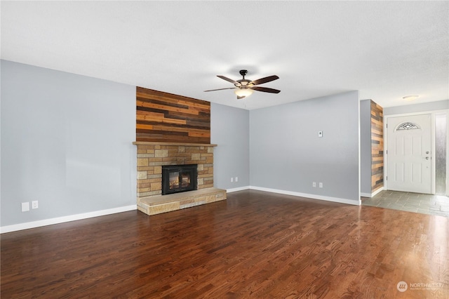 unfurnished living room featuring baseboards, a stone fireplace, wood finished floors, and a ceiling fan