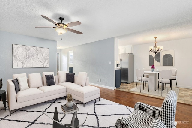 living room with light wood finished floors, ceiling fan with notable chandelier, a textured ceiling, and baseboards