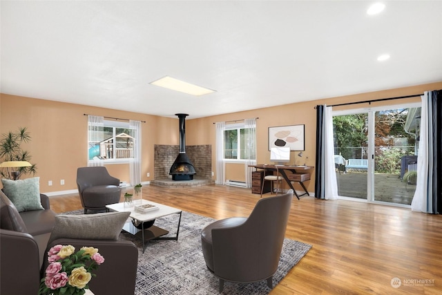 living room featuring baseboards, light wood-type flooring, recessed lighting, a wood stove, and a baseboard radiator