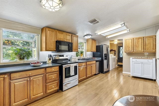 kitchen with washing machine and dryer, visible vents, appliances with stainless steel finishes, light wood-type flooring, and dark countertops