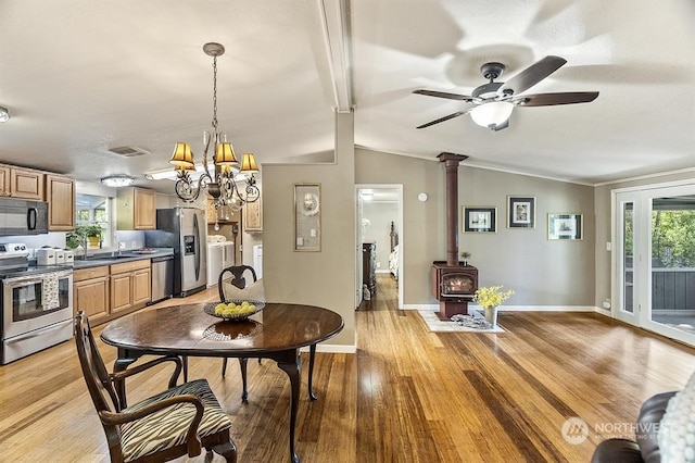 dining room with a wood stove, light wood-style flooring, baseboards, and vaulted ceiling