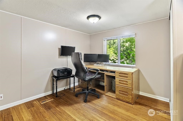 office space featuring a textured ceiling, light wood finished floors, visible vents, and baseboards