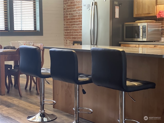 bar with wood-type flooring, appliances with stainless steel finishes, and wooden walls