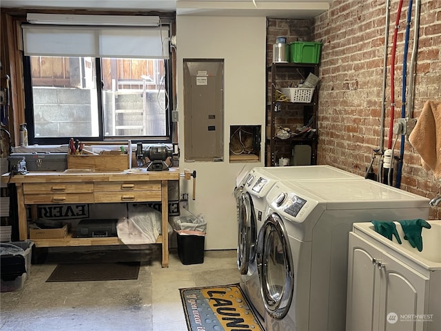 clothes washing area featuring electric panel, independent washer and dryer, and brick wall