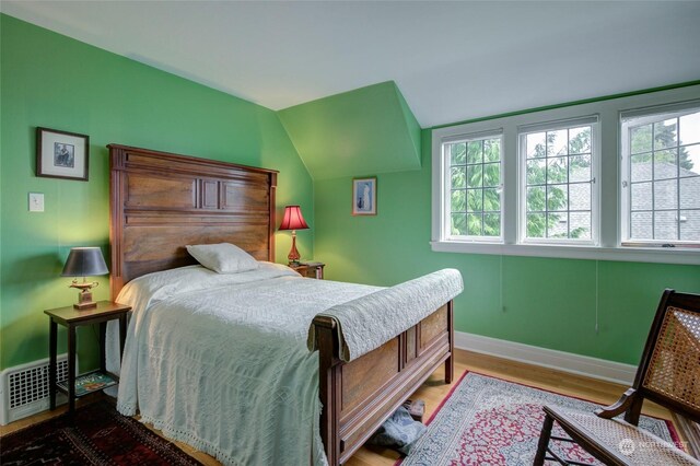 bedroom with vaulted ceiling, hardwood / wood-style floors, and multiple windows