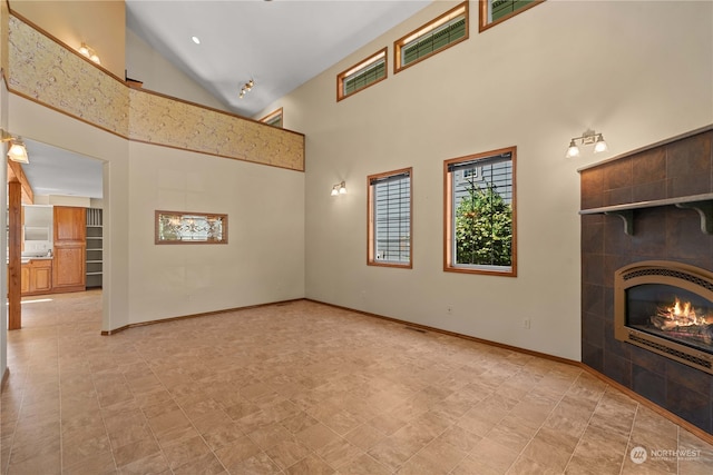 unfurnished living room with high vaulted ceiling and a tile fireplace