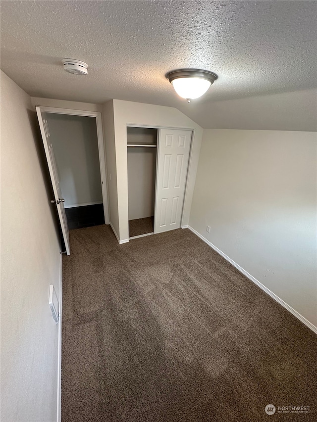 unfurnished bedroom featuring a textured ceiling, carpet, lofted ceiling, and a closet