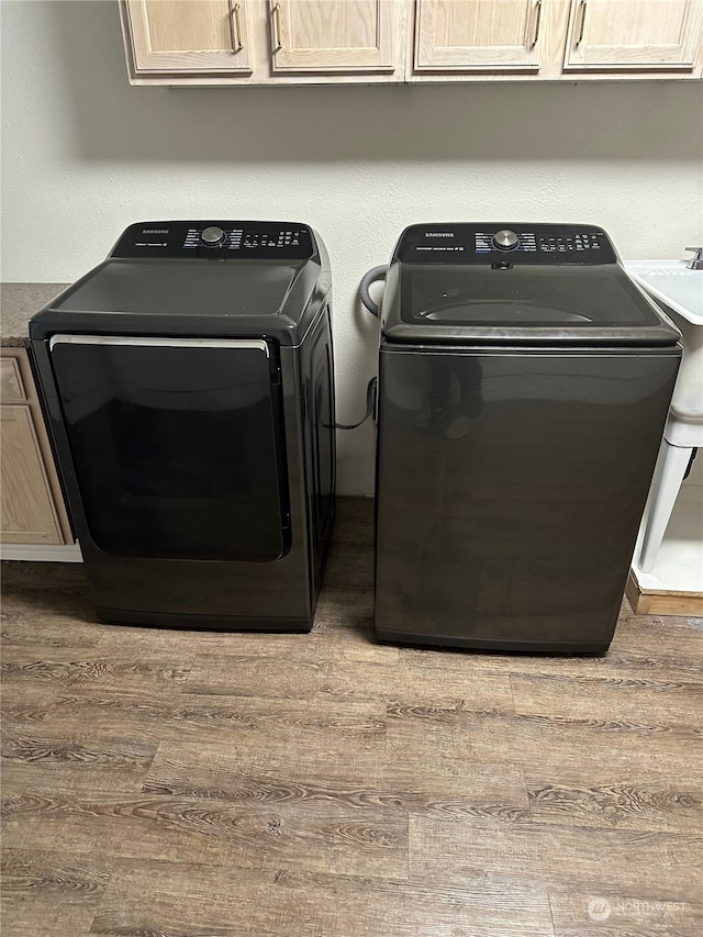 clothes washing area with wood-type flooring, cabinets, and washing machine and clothes dryer