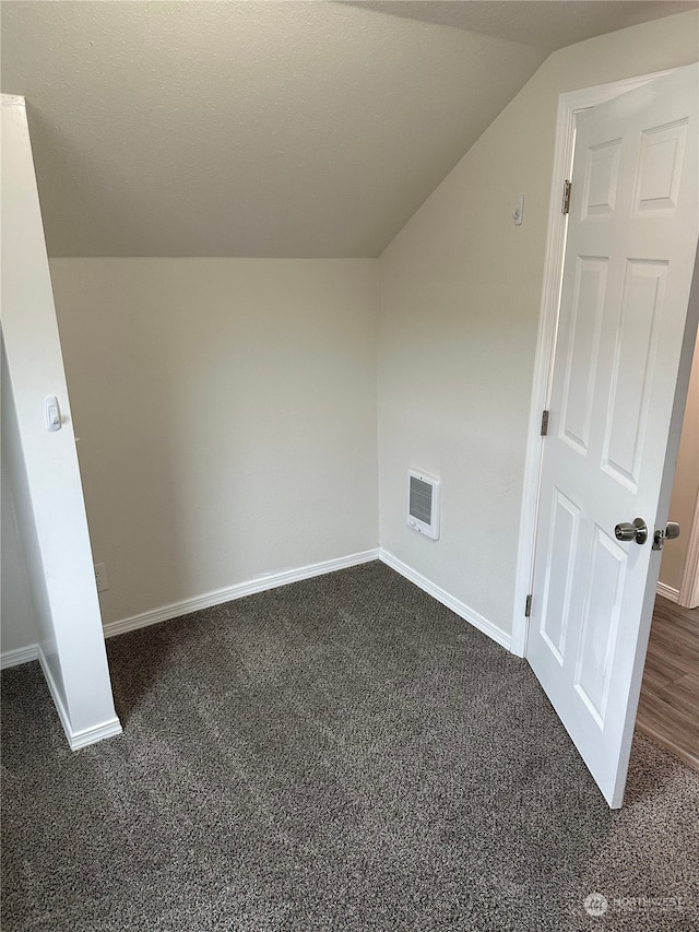 additional living space featuring dark carpet and vaulted ceiling