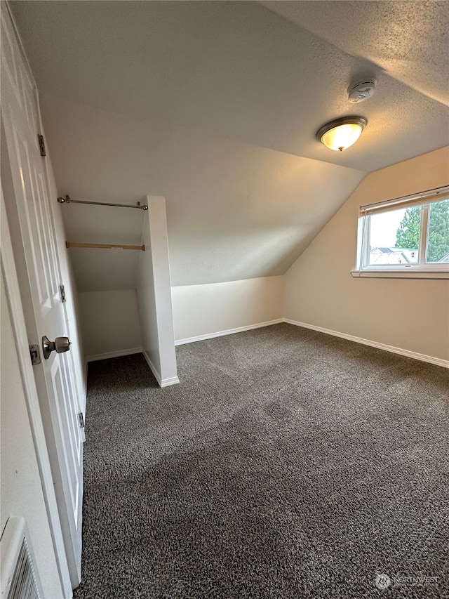 bonus room featuring a textured ceiling, lofted ceiling, and dark carpet