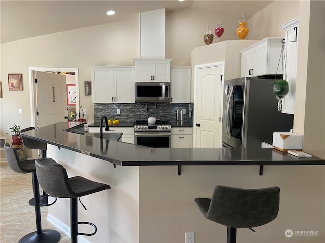 kitchen with appliances with stainless steel finishes, vaulted ceiling, a kitchen bar, and white cabinets