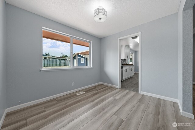 spare room featuring a textured ceiling and light hardwood / wood-style floors