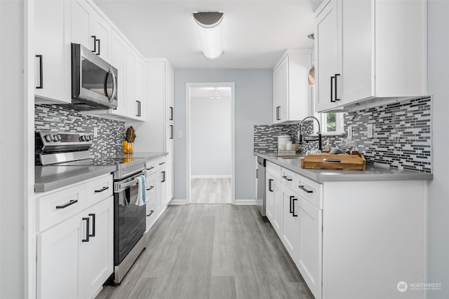 kitchen with light hardwood / wood-style flooring, backsplash, appliances with stainless steel finishes, sink, and white cabinets